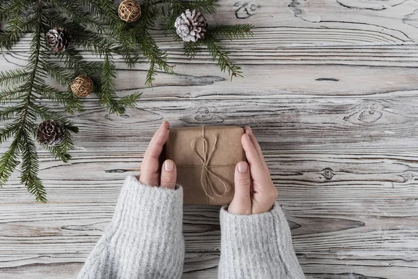 Female packing gifts. Cardboard box in craft paper, christmas rope and tree on the rustic wood planks background. DIY.