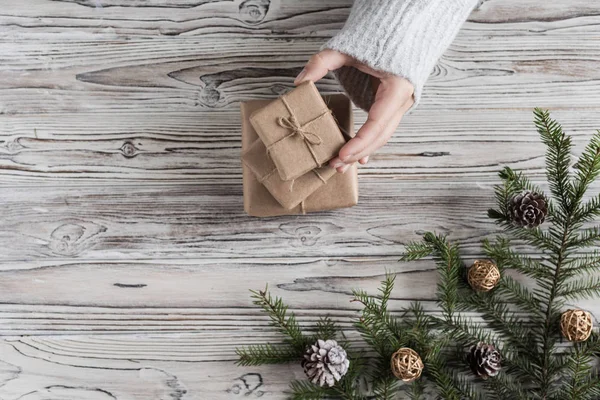 Female packing gifts. Cardboard box in craft paper, christmas rope and tree on the rustic wood planks background. DIY.