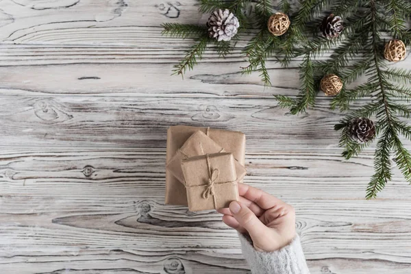 Female packing gifts. Cardboard box in craft paper, christmas rope and tree on the rustic wood planks background. DIY.