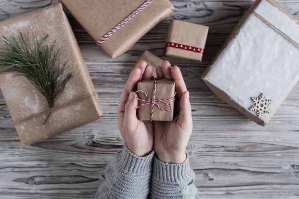 Female packing small gift. Cardboard box in craft paper, christmas rope and tree on the rustic wood planks background. DIY.