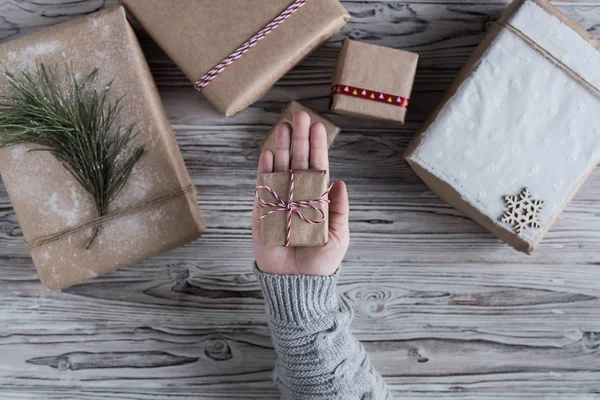 Female packing small gift. Cardboard box in craft paper, christmas rope and tree on the rustic wood planks background. DIY.