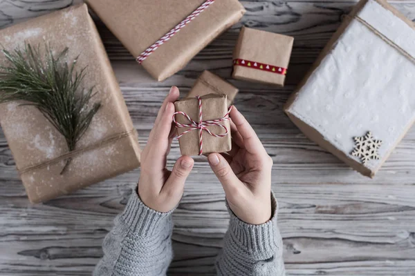 Female packing small gift. Cardboard box in craft paper, christmas rope and tree on the rustic wood planks background. DIY.