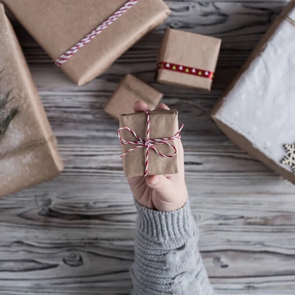 Female packing small gift. Cardboard box in craft paper, christmas rope and tree on the rustic wood planks background. DIY.