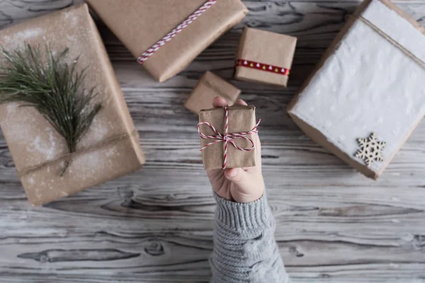 Female packing small gift. Cardboard box in craft paper, christmas rope and tree on the rustic wood planks background. DIY.