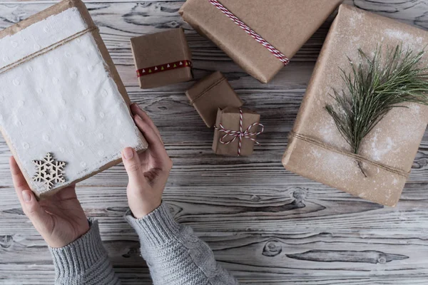 Female packing gifts. Cardboard box in craft paper, christmas rope and tree on the rustic wood planks background. DIY.