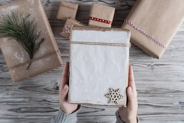 Female packing gifts. Cardboard box in craft paper, christmas rope and tree on the rustic wood planks background. DIY.