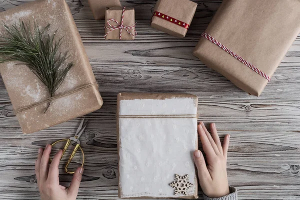 Female packing gifts. Cardboard box in craft paper, christmas rope and tree on the rustic wood planks background. DIY.