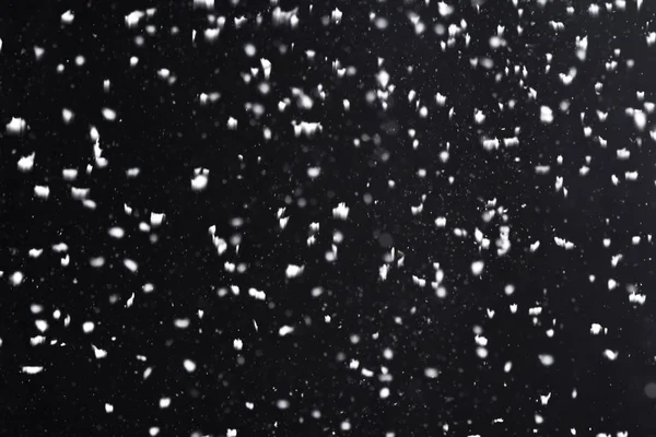 Falling  snow at night. Bokeh lights on black background, flying snowflakes in the air. Overlay texture. Snowstorm