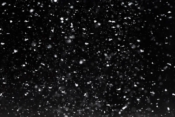 Falling  snow at night. Bokeh lights on black background, flying snowflakes in the air. Overlay texture. Snowstorm