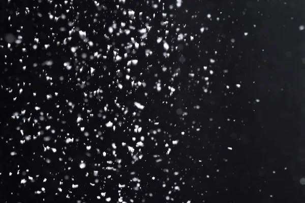 Falling  snow at night. Bokeh lights on black background, flying snowflakes in the air. Overlay texture. Snowstorm