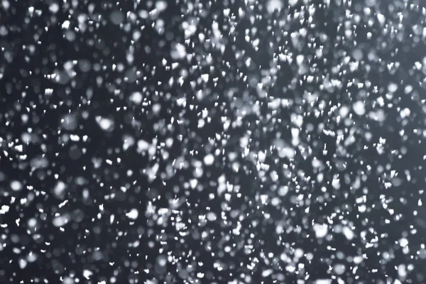 Falling  snow at night. Bokeh lights on black background, flying snowflakes in the air. Overlay texture. Snowstorm