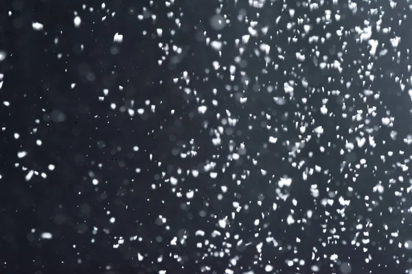 Falling  snow at night. Bokeh lights on black background, flying snowflakes in the air. Overlay texture. Snowstorm