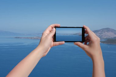 Kadın cep telefonuyla Yunan adasının manzarasını çekiyor. Üst Manzara. Akıllı telefondan deniz ve dağ manzarası