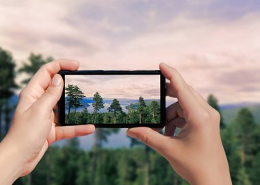 Norveç 'te cep telefonuyla çekilmiş orman fotoğrafı. Dişi, dağdaki resim ağaçlarını çekiyor ve akıllı telefondaki gölün arka planında....