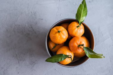 Gri beton arka plandaki küçük demir kovada Mandarinler