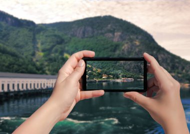 Norveç 'teki Florli köyünün fotoğrafı cep telefonunda. Kadın, Lysefjorden 'da akıllı telefondan resim ve liman alıyor..