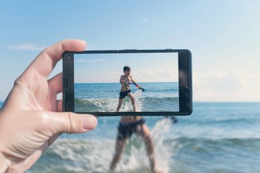Kadın, sahilde telefonla bir çocuğun fotoğrafını çekiyor.