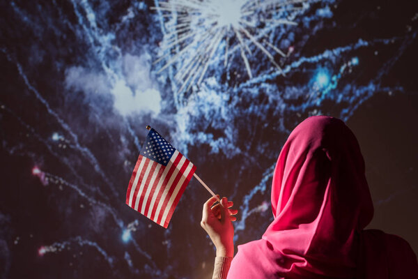 Muslim woman in a scarf holding American flag during fireworks at night. — Stock Image Muslim Woman Scarf Holding American Flag Fireworks Night Stock Image