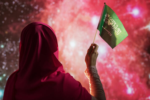 Muslim woman in a scarf holding flag of Saudi Arabia during fireworks at night. — Stock Image Muslim Woman Scarf Holding Flag Saudi Arabia Fireworks Night Stock Picture