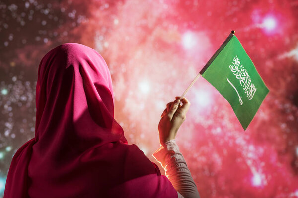 Muslim woman in a scarf holding flag of Saudi Arabia during fireworks at night. — Stock Image Muslim Woman Scarf Holding Flag Saudi Arabia Fireworks Night Royalty Free Stock Photos
