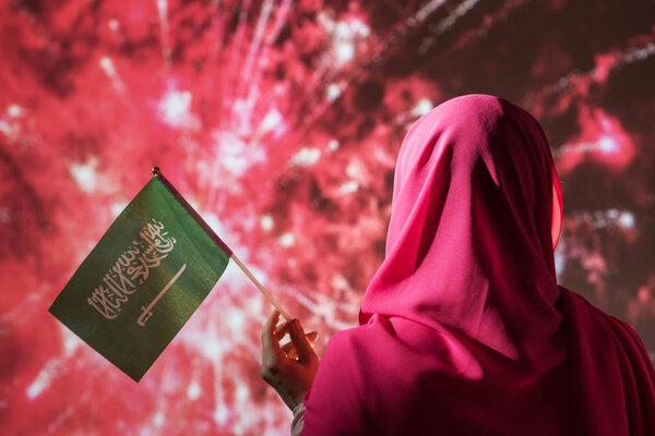 Muslim woman in a scarf holding flag of Saudi Arabia during fireworks at night. — Stock Image Muslim Woman Scarf Holding Flag Saudi Arabia Fireworks Night Stock Photo