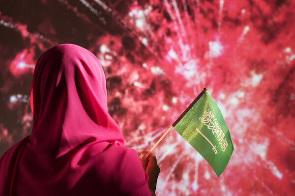 Muslim woman in a scarf holding flag of Saudi Arabia during fireworks at night. — Stock Image Muslim Woman Scarf Holding Flag Saudi Arabia Fireworks Night Stock Photo