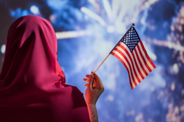 Muslim woman in a scarf holding American flag during fireworks at night. — Stock Image Muslim Woman Scarf Holding American Flag Fireworks Night Stock Image