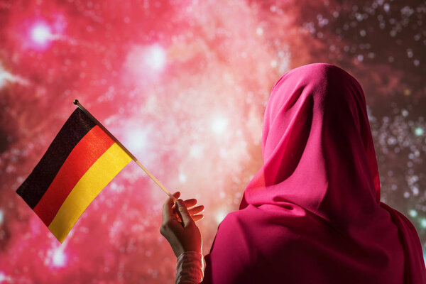 Muslim woman in a scarf holding flag of German during fireworks at night. — Stock Image Muslim Woman Scarf Holding Flag German Fireworks Night Royalty Free Stock Photos