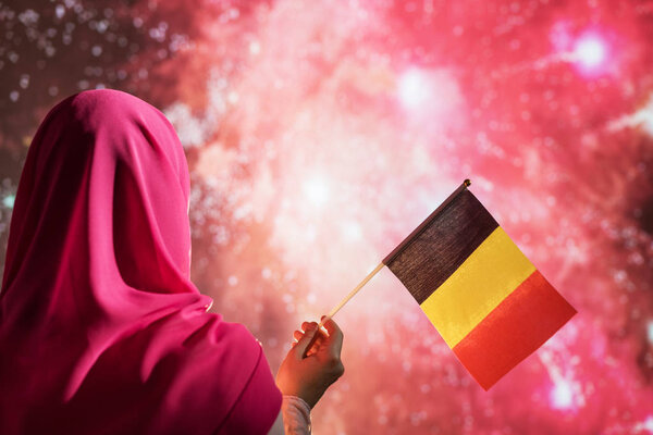Muslim woman in a scarf holding flag of Belgium during fireworks at night. — Stock Image Muslim Woman Scarf Holding Flag Belgium Fireworks Night Stock Picture