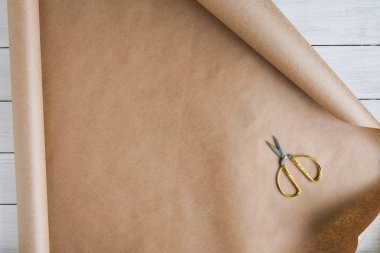 Dişi eller, tahta beyaz masaya hediye ve çiçek paketlemek için bir rulo kahverengi el işi kağıt açıyor. Boşluğu kopyala. 