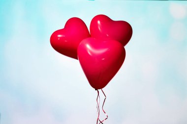 Gökyüzünde kalp şeklinde üç kırmızı balon mavi pastel renkte arka planda. Sevgililer Günü konsepti.