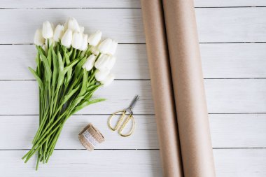 Tahta masanın üzerinde beyaz lale demetini el işi kağıtlara sarmak. Düz yatıyordu