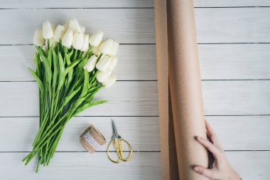 Çiçekçi kadın, ahşap masaya beyaz laleleri el işi kağıtlara sarıyordu. Düz yatıyordu