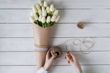 Çiçekçi kadın, ahşap masaya beyaz laleleri el işi kağıtlara sarıyordu. Düz yatıyordu