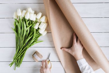 Çiçekçi kadın, ahşap masaya beyaz laleleri el işi kağıtlara sarıyordu. Düz yatıyordu
