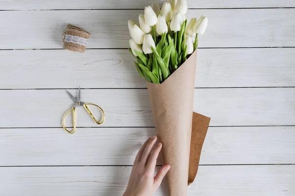 木製のテーブルの上にパッククラフト紙に白いチューリップの美しい花束を包む女性花屋 — ストック写真