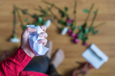hand of woman with crumpled paper of letter among scattered flowers. Broken relationships in bad Valentine's day. concept.