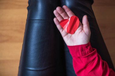 woman with crumpled paper heart in the hand sitting on the floor.  Broken relationships in bad Valentine's day. concept. Top view