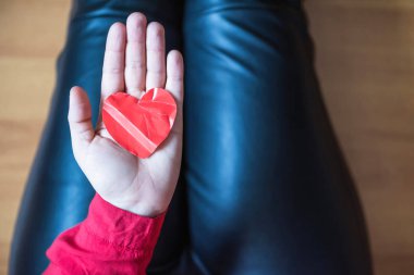 woman with crumpled paper heart in the hand sitting on the floor.  Broken relationships in bad Valentine's day. concept. Top view