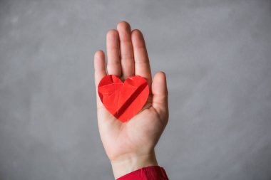 woman hand with crumpled paper red heart against the concrete floor.  Broken relationships in bad Valentine's day. concept.