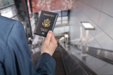 Havaalanı yürüyen merdiveninde elinde Amerikan pasaportu olan mavi elbiseli bir adam. 