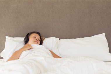 Kulaklıklı güzel bir kadın yatak odasındaki yatakta uzanmış müzik dinliyor. Gözleri kapalı, sakin bir yüzü ve örtülü bir çarşafı var.. 