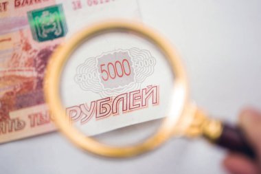 Banknote of five thousand russian rubles under a magnifying glass in the human hand. Concept clipart