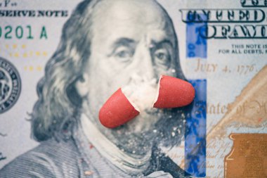 Kırmızı hapın iki yarısı Ben Franklin 'in yüz dolarlık banknotunun yüzünde yatıyor. Konsept.
