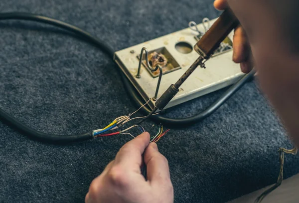 Close-up of person hands and soldering iron, tool and wires. Soldering process at home