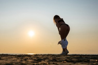Halk plajında kumsalda duran ve çamaşırlarını çıkaran bir kadın. Gün batımı. Yaz konsepti.