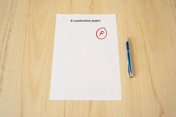 Examination paper with grade test results. Failed university exam with pen on the school desk. Copyspace. Mockup. Flat lay
