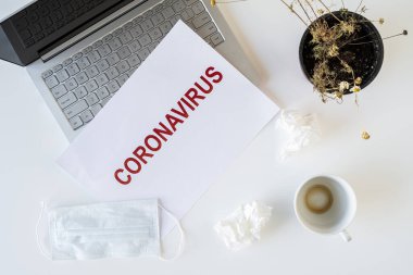 Coronavirus ve karantina yüzünden ofiste hasta bir çalışanın terkedilmiş işyeri. Tıbbi maske, peçete ve bir fincan bitmiş kahve ile birlikte. Dünya çapında salgın konsepti