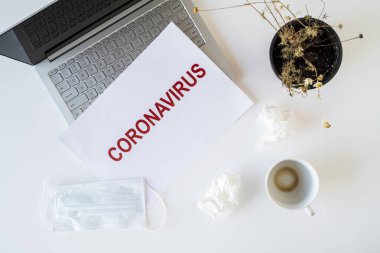 Coronavirus ve karantina yüzünden ofiste hasta bir çalışanın terkedilmiş işyeri. Tıbbi maske, peçete ve bir fincan bitmiş kahve ile birlikte. Dünya çapında salgın konsepti