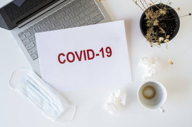 Coronavirus ve karantina yüzünden ofiste hasta bir çalışanın terkedilmiş işyeri. Tıbbi maske, peçete ve bir fincan bitmiş kahve ile birlikte. Dünya çapında salgın konsepti
